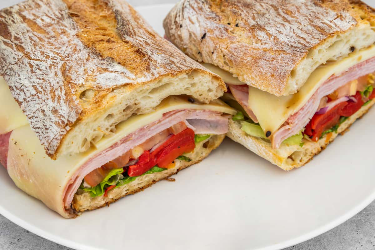 Toasted ciabatta sandwich stacked with ham, turkey, Swiss cheese, lettuce, tomato, and roasted red peppers.