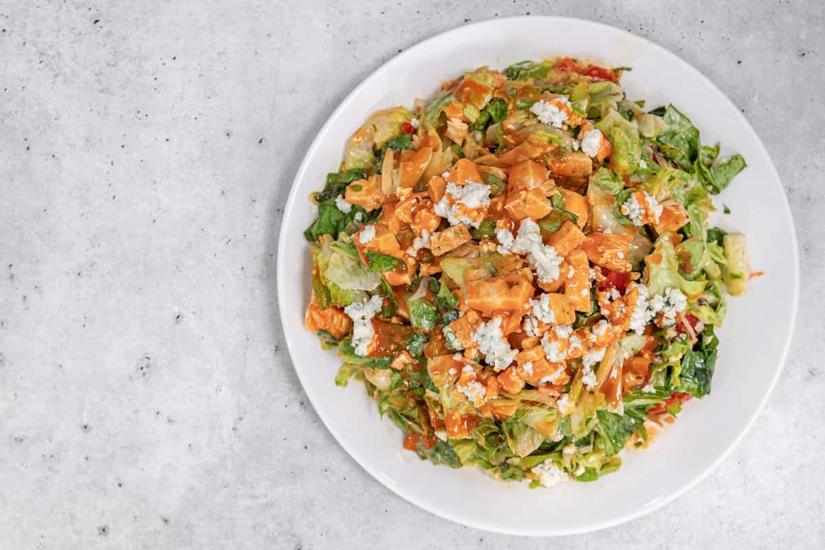 Buffalo chicken salad with romaine lettuce, blue cheese crumbles, and spicy buffalo sauce on a white plate.
