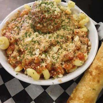 cavatappi pasta with tomato sauce, topped with a meatball and parmesan cheese with parsley as a garnish and served with a breadstick