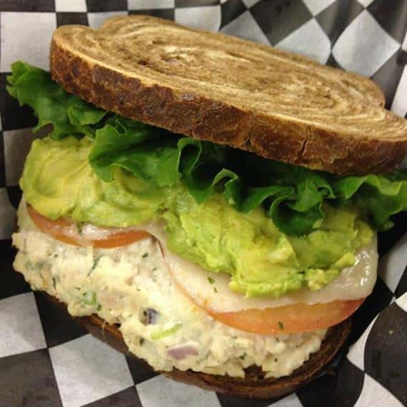 chicken salad sandwich with lettuce, tomato, cheese, and avocado on marble rye bread
