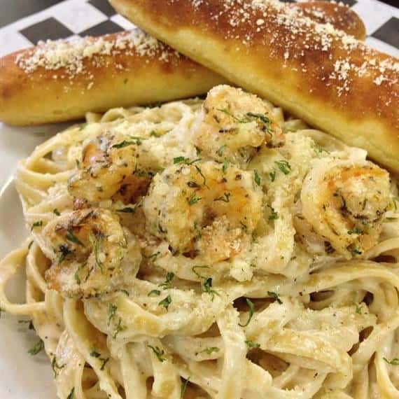 linguine pasta with shrimp, topped with parmesan cheese and parsley as a garnish. served with breadsticks