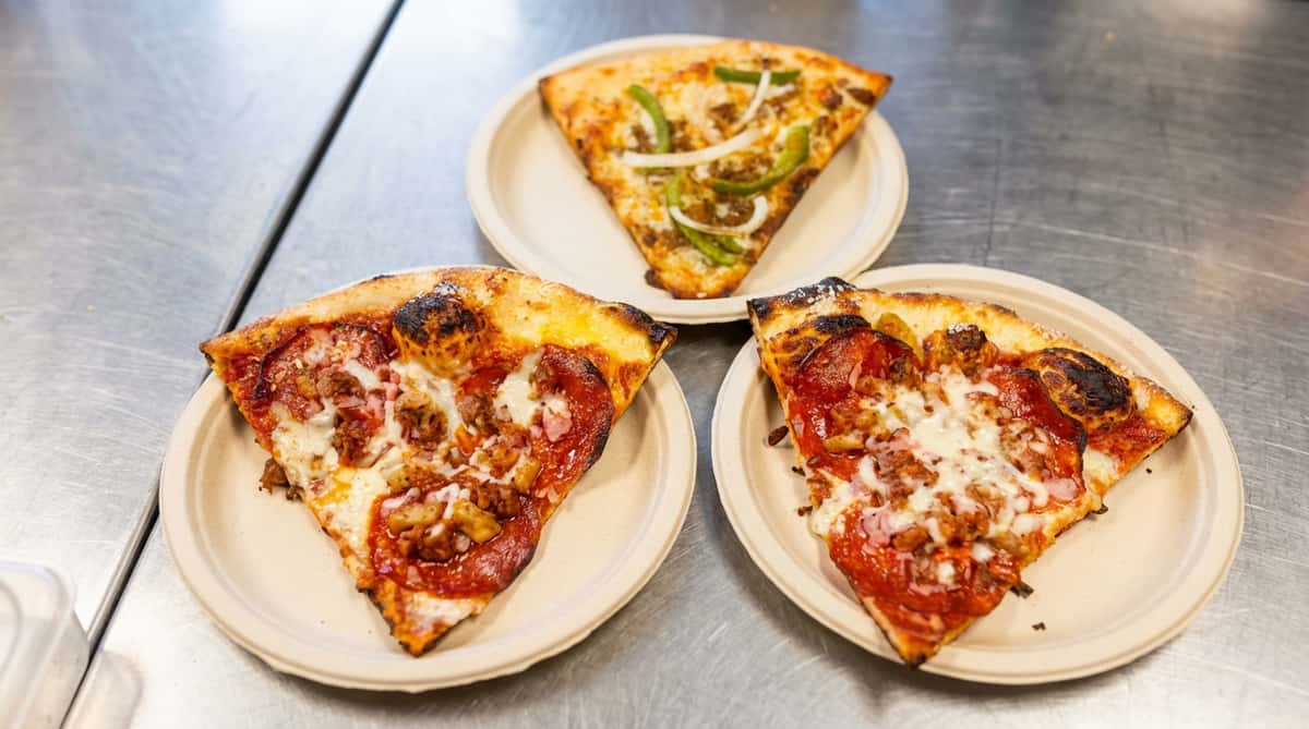 Three pizza slices on beige plates atop a metal surface: two pepperoni and sausage, one with green peppers and onions.