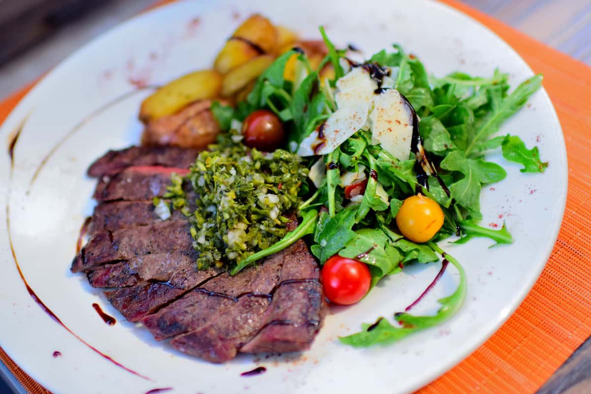 Mesquite Grilled Hanger Steak sliced and served with chimichurri, over Arugula, heirloom cherry tomatoes, shaved parmesan cheese and roasted potatoes