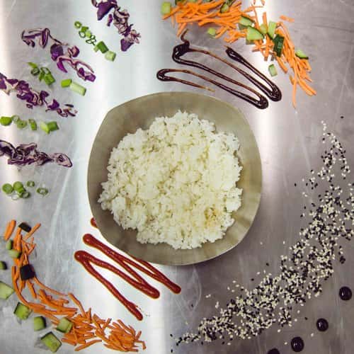 Bowl of white rice with assorted spices on a metal counter-top