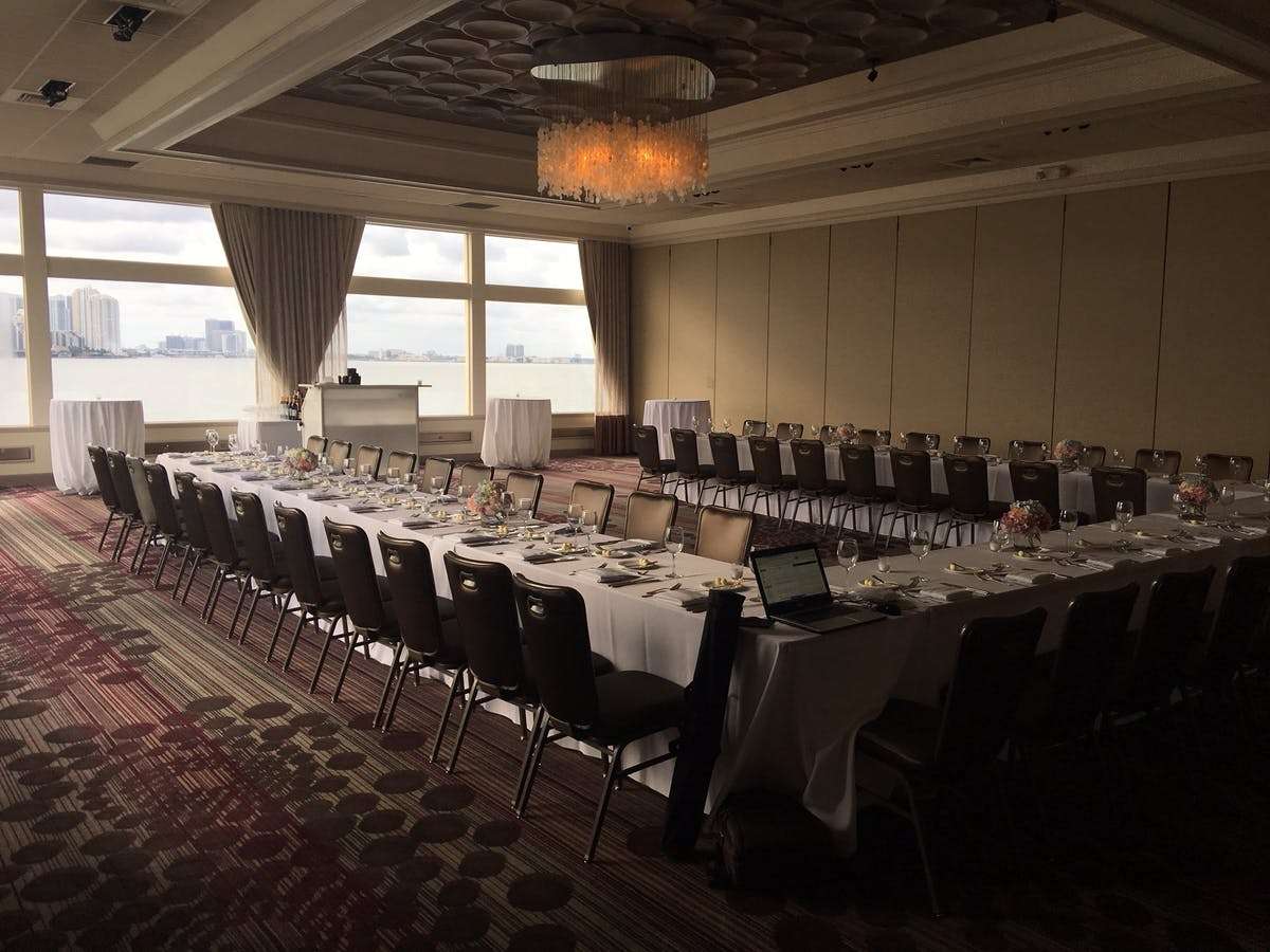 Upscale banquet room with formal event table layout, chandelier lighting, and panoramic waterfront views