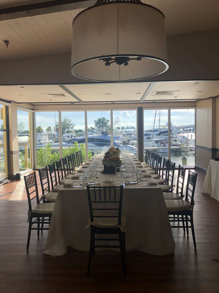 Elegant waterfront private dining setup with long banquet table and panoramic marina yacht views for upscale events