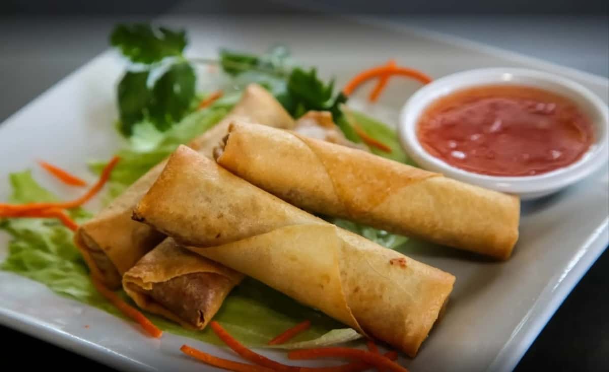 Four golden-brown fried spring rolls served on a plate with a side of sweet chili dipping sauce