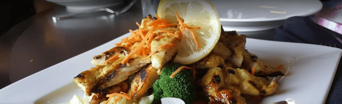 Slices of grilled chicken garnished with a large lemon slice and broccoli