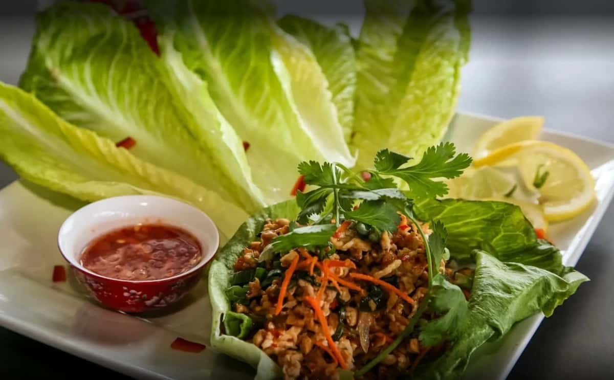 A dish of minced meat salad served with large, fresh green lettuce leaves for wrapping