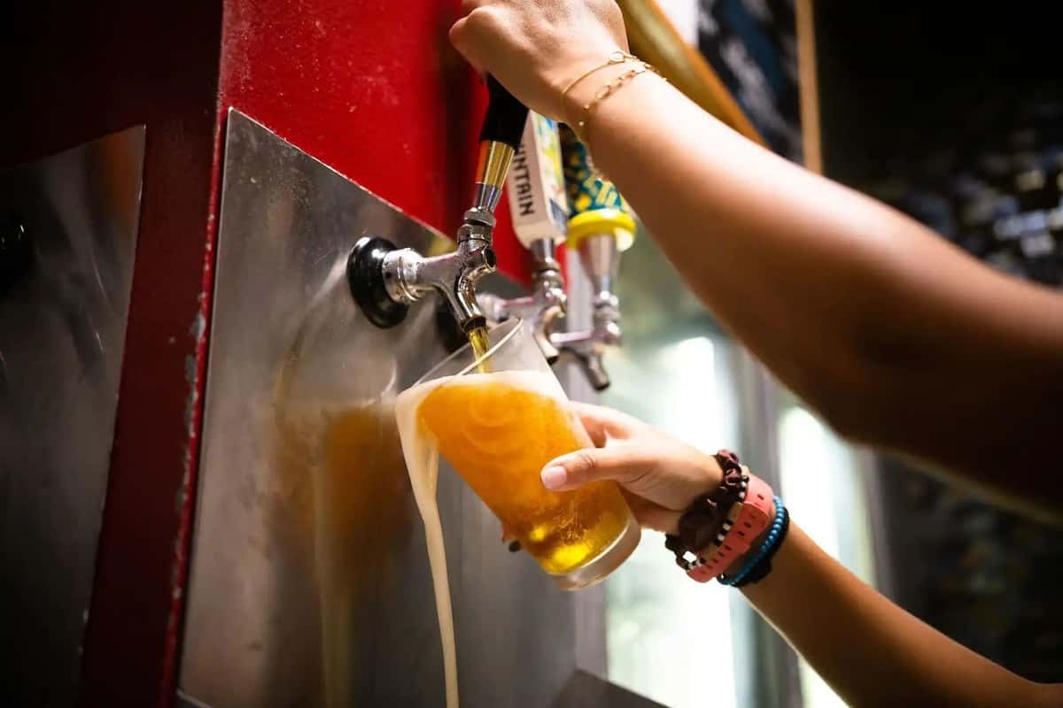 Bartender pouring golden draft beer from tap into a glass at a lively bar