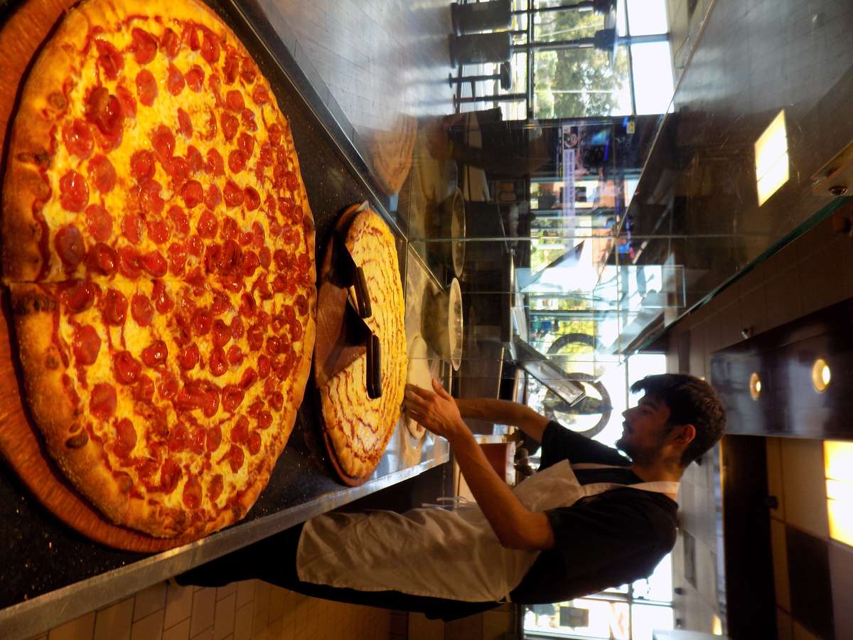 pizza chef preparing large pepperoni pizzas behind glass counter in a casual pizzeria kitchen