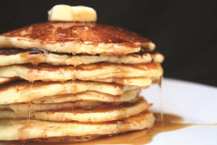 tall stack of pancakes topped with butter and syrup