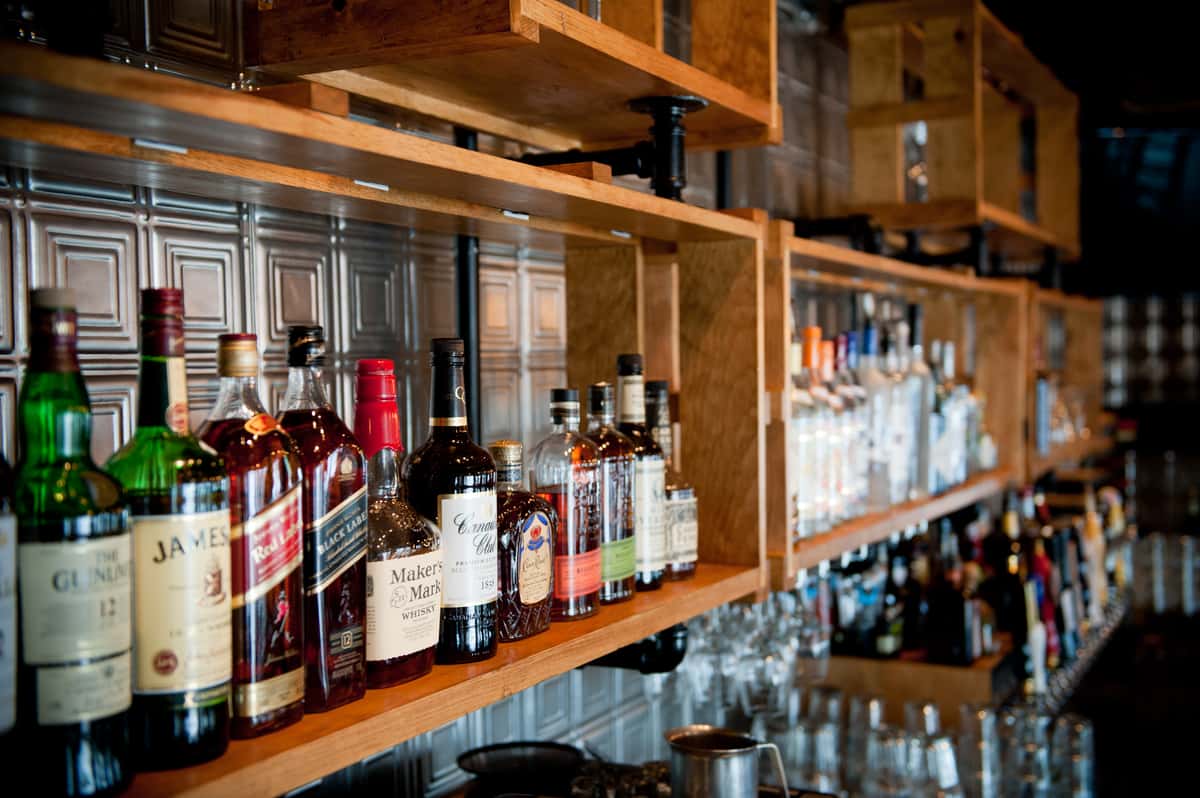 Bar shelves with assorted whiskey, bourbon, and liquor bottles in a warm rustic restaurant setting