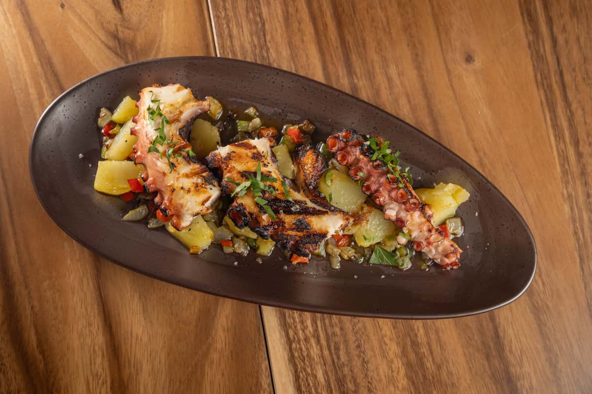 A dish of chopped grilled octopus mixed with potatoes and peppers on a dark plate.