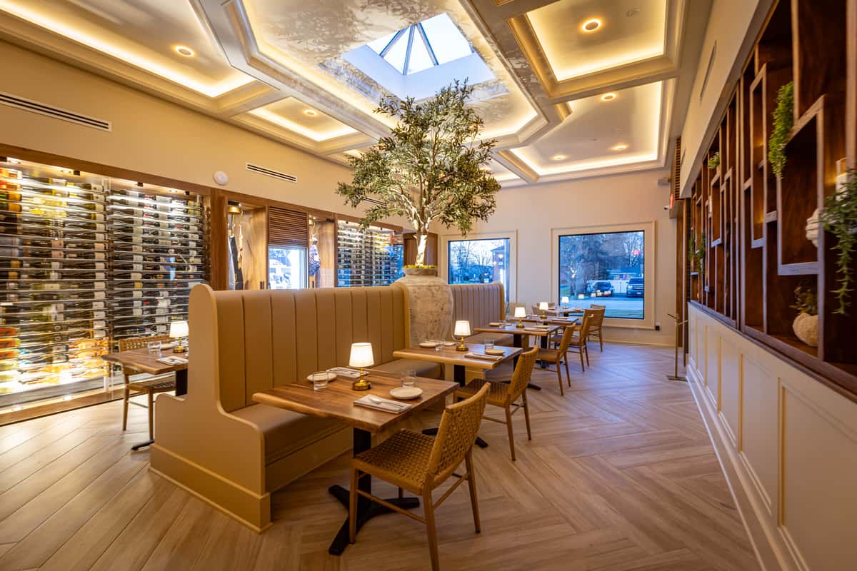 A view of a restaurant dining space with beige booth seating, wooden tables, and geometric ceiling lights.