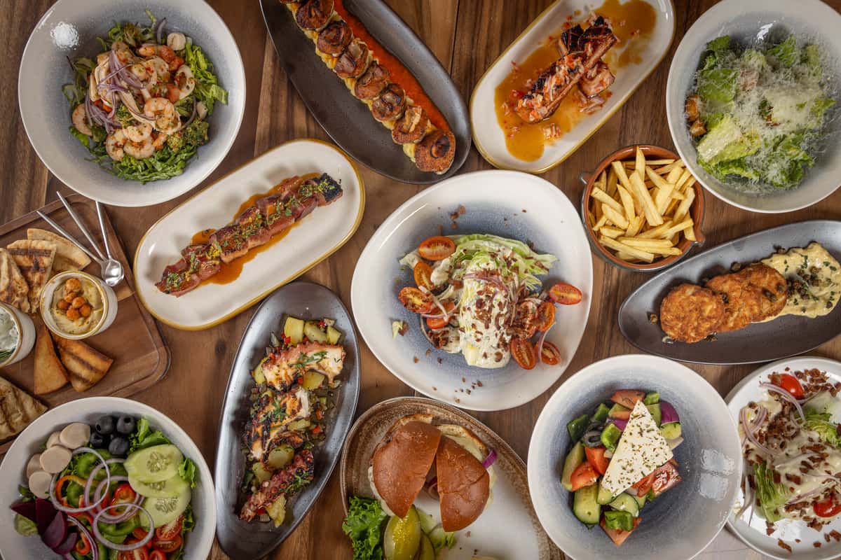 An overhead shot of a dining table crowded with various dishes, including salads, calamari, and sandwiches.