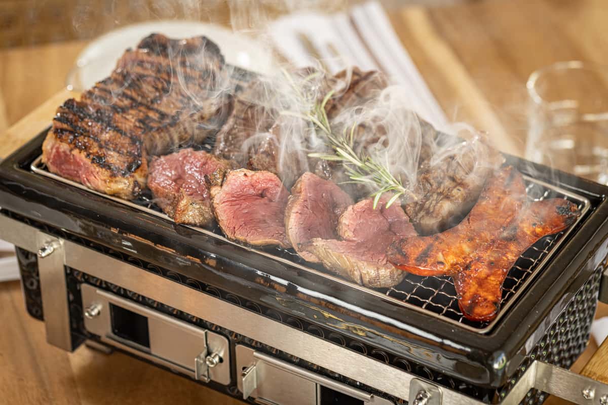 A small personal grill (hibachi style) cooking steak pieces at the table, emitting smoke.