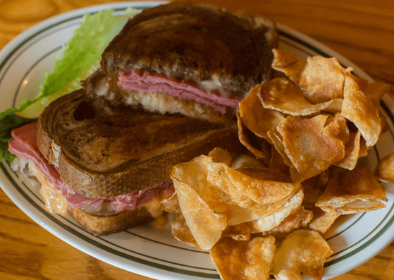 ham sandwich with melted cheese and potato chips on the side