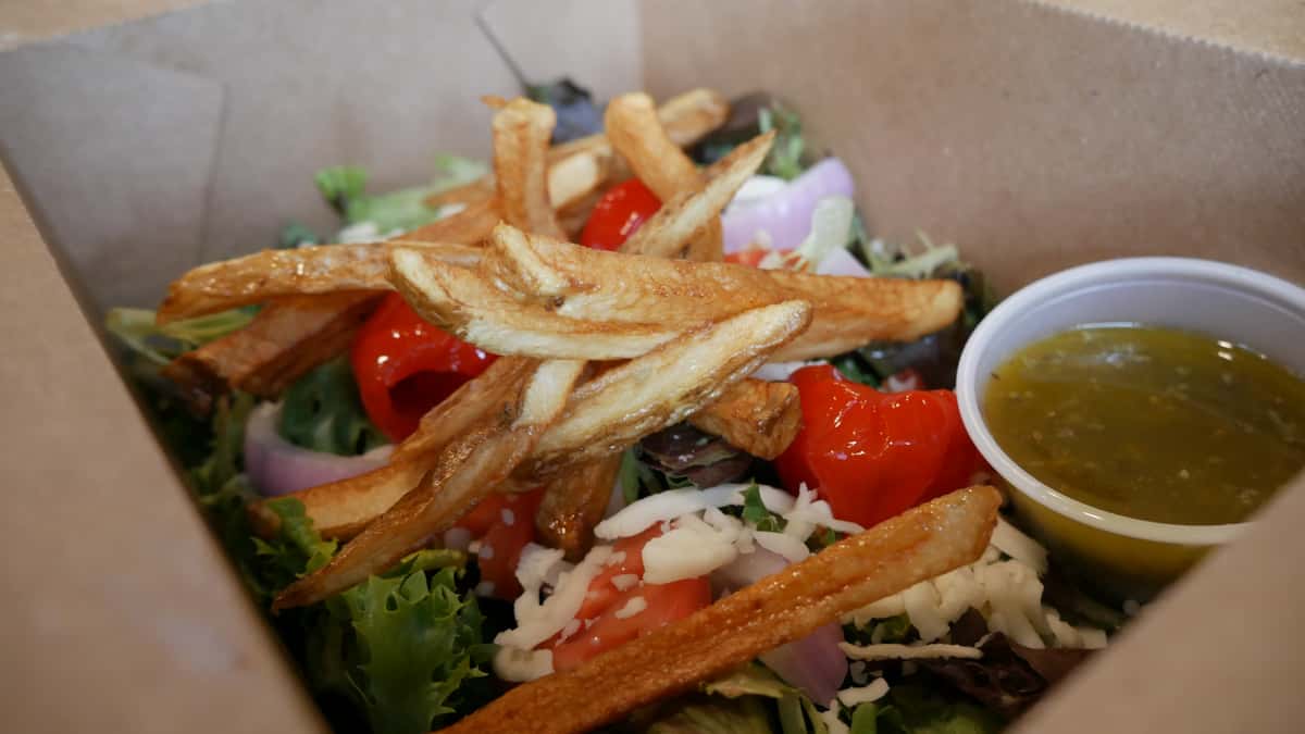 Salad with fries on top and a side of dressing