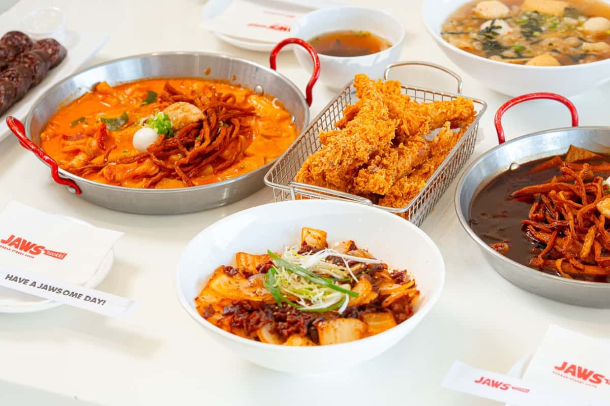 Assorted Korean dishes including spicy tteokbokki, fried chicken strips, and noodle soup served on a white table.