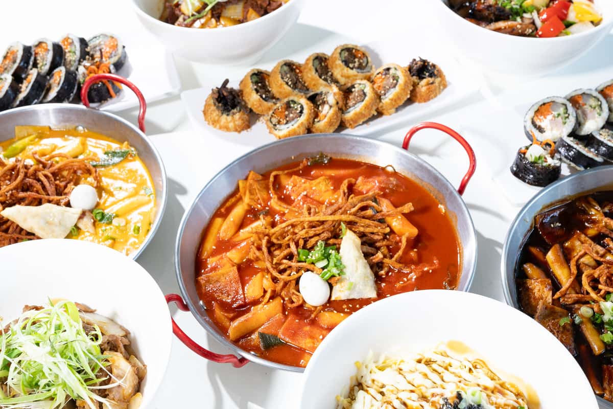 Variety of Korean dishes including spicy tteokbokki, fried gimbap, and rice bowls arranged on a white table.