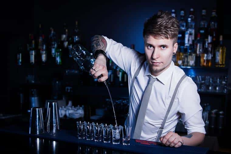 Bartender pouring alcohol into shot glasses behind the bar