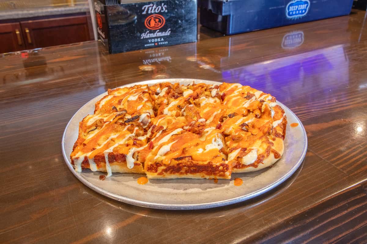 Buffalo chicken pizza with melted cheese, drizzled sauce, and crispy chicken pieces on a golden crust served on a metal tray