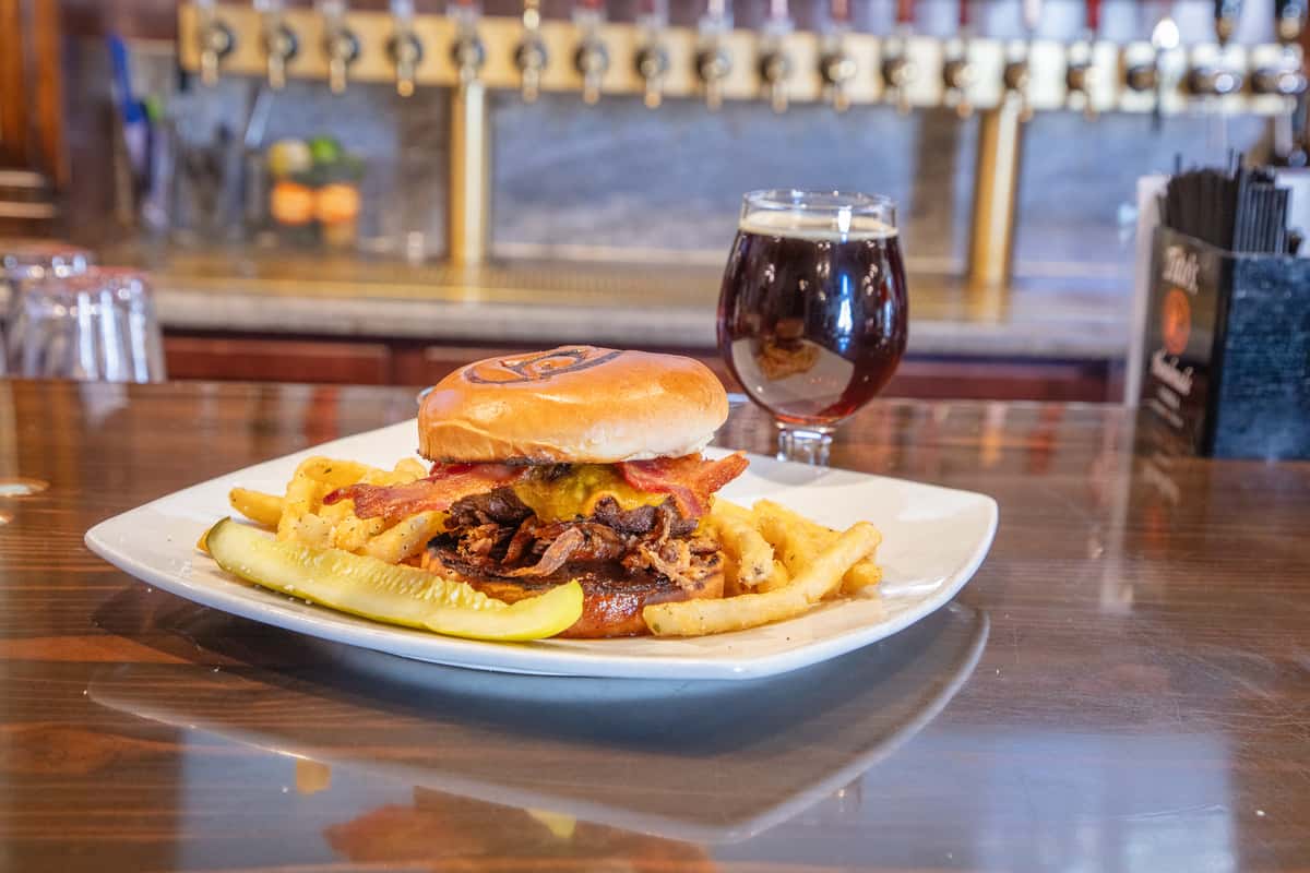 Smokehouse burger with bacon, cheese, and fries served with craft beer on a bar counter