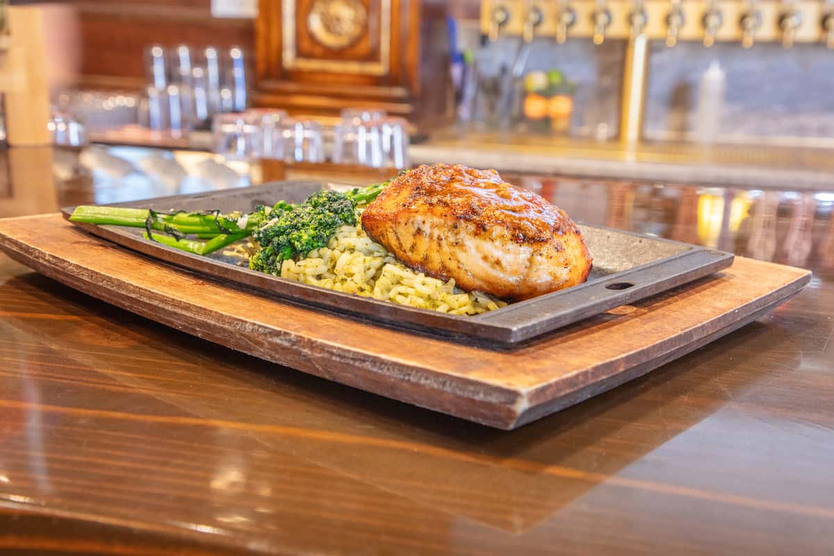 Grilled salmon fillet served over seasoned grains with broccolini on a hot stone platter at a modern brewery restaurant