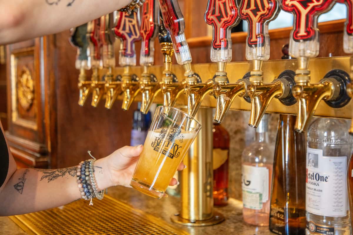 Fresh draft beer being poured into a branded pint glass from polished brass taps at a craft brewery bar