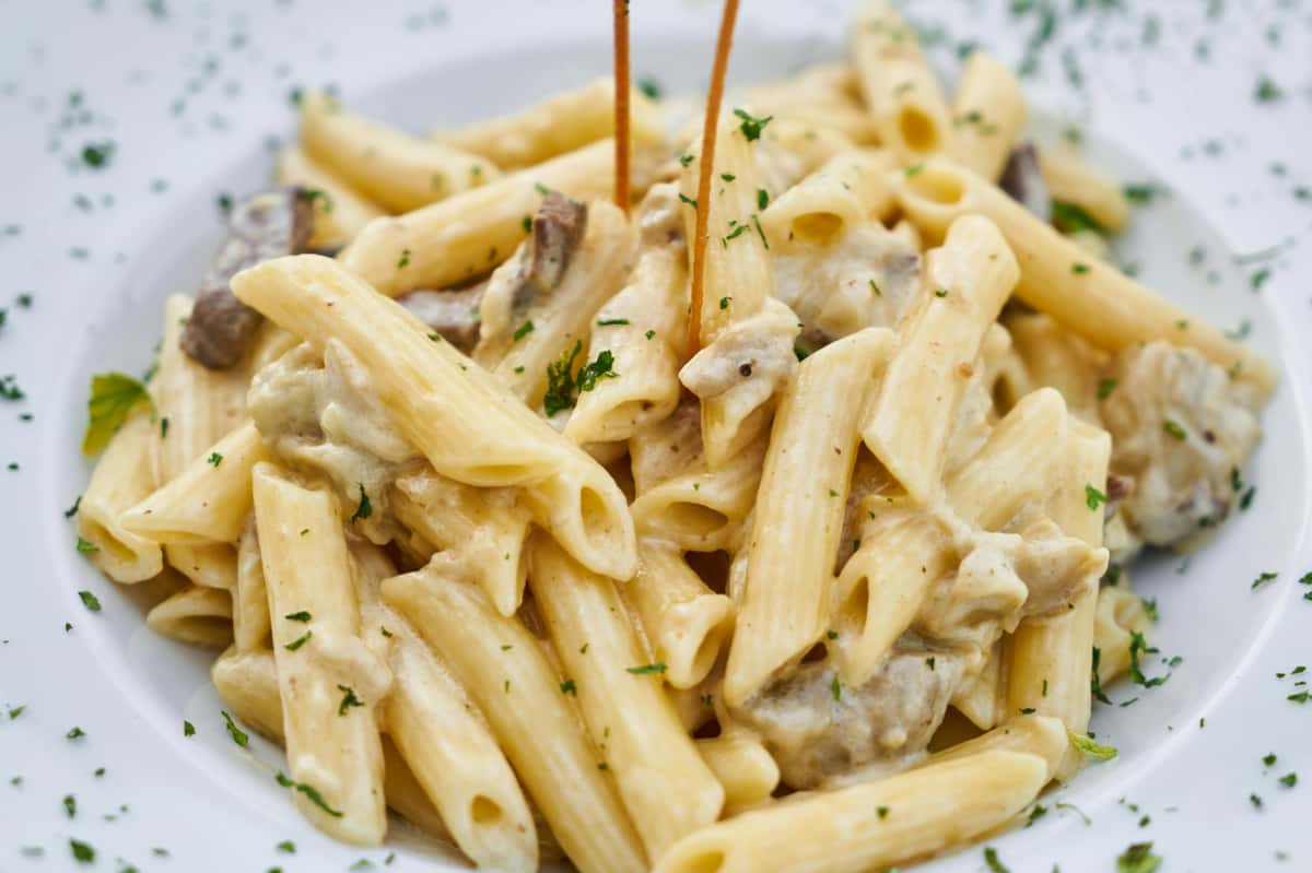Creamy penne pasta with mushrooms in a white sauce, garnished with chopped parsley on a white plate.