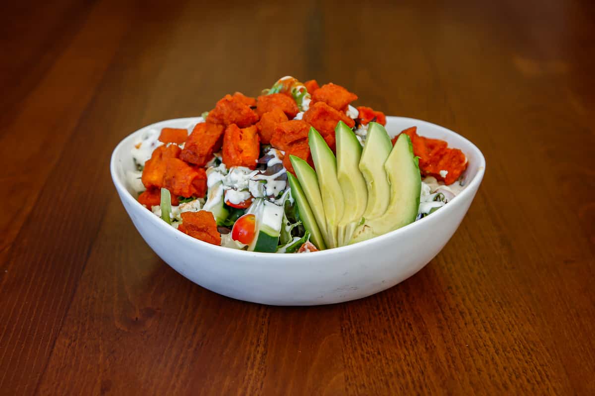 Buffalo chicken salad with avocado, fresh vegetables and crumbled cheese