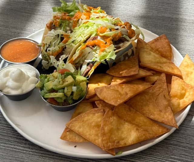 Plate of crispy tortilla chips with a loaded taco salad, guacamole, sour cream, and salsa on the side