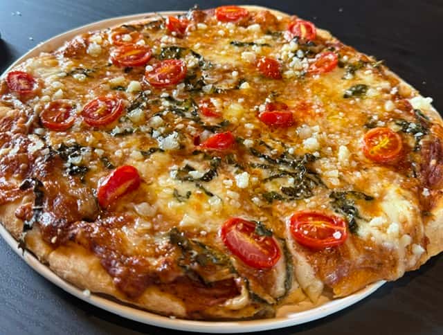 Thin-crust pizza topped with cherry tomatoes, fresh basil, and crumbled cheese