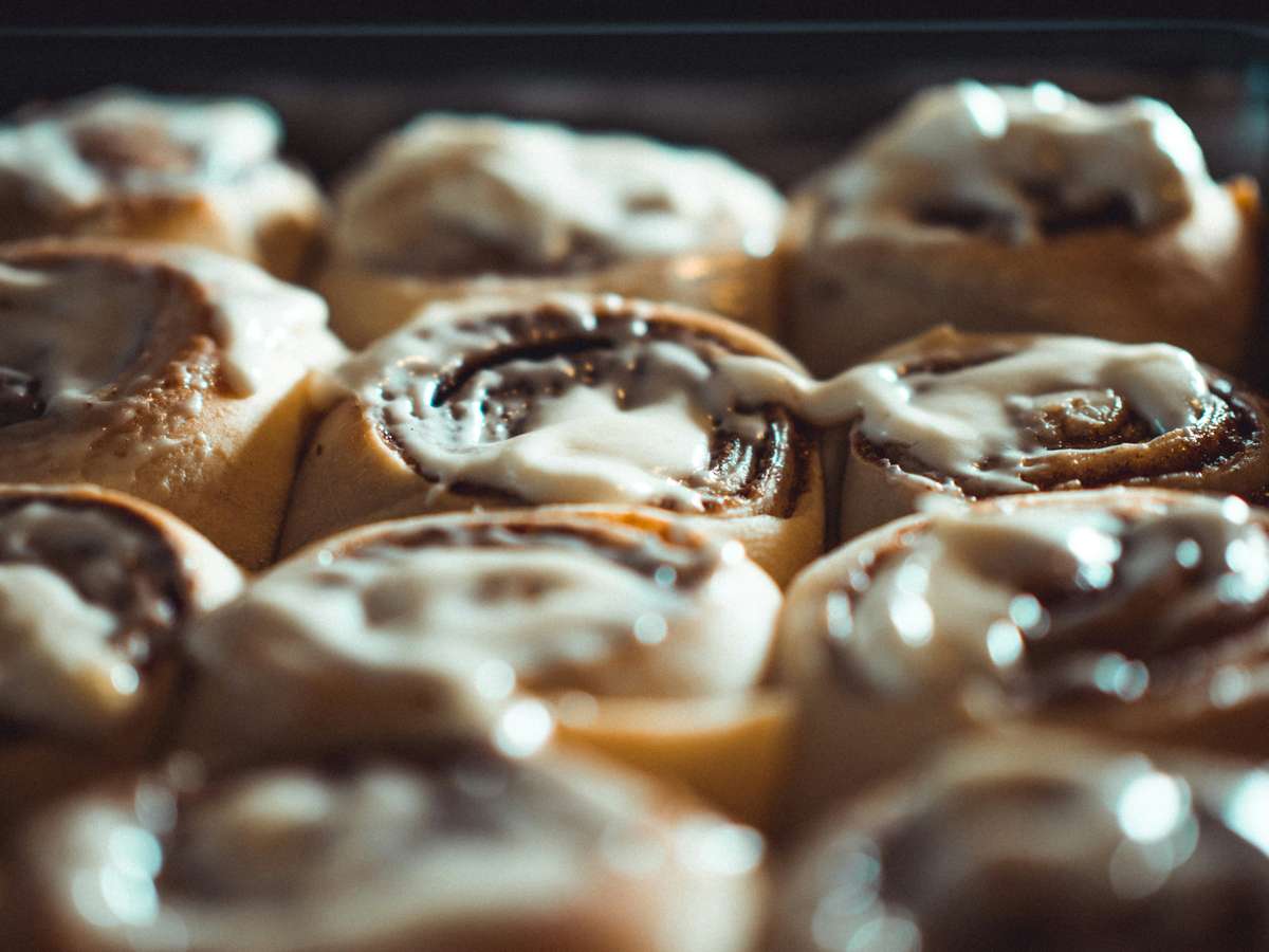 Close-up of freshly baked cinnamon rolls topped with icing in a baking tray.