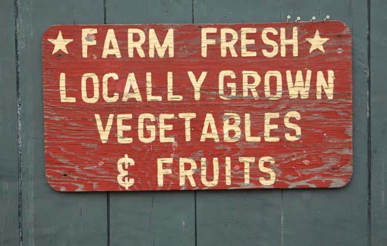 Wood painted sign on wall reading Farm Fresh locally grown vegetables and fruits.