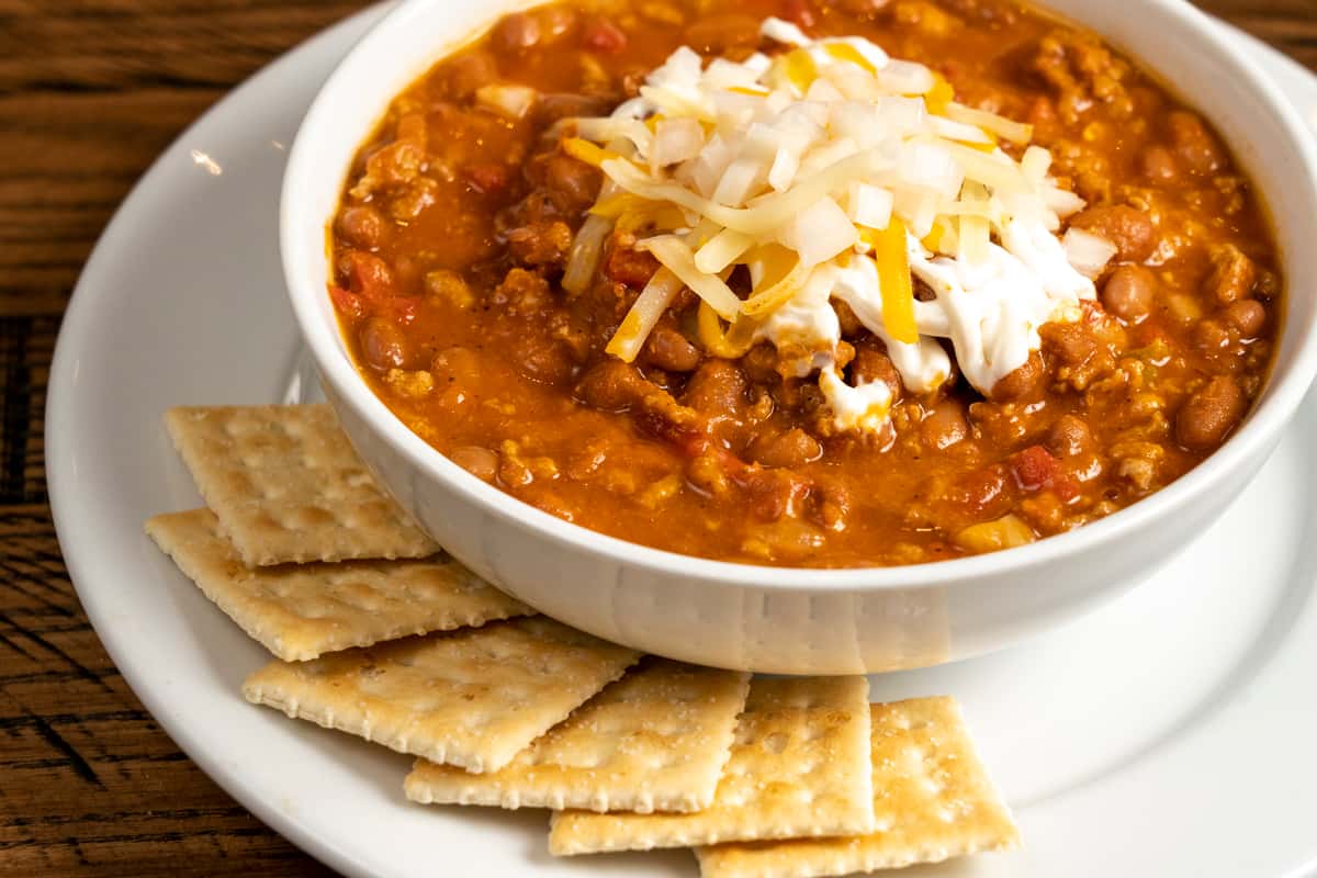 Bowl of Chili with saltine crackers topped with shredded cheese and sour cream