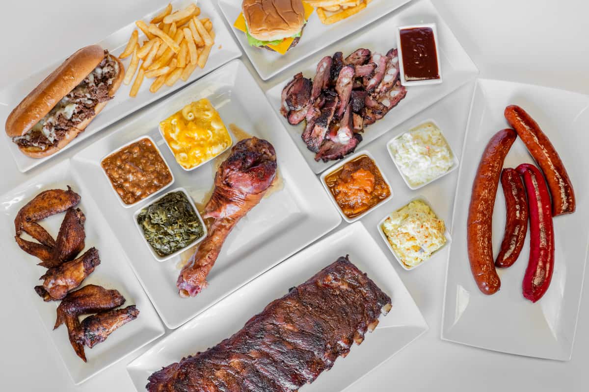 Overhead view of a BBQ feast featuring smoked ribs, brisket, and an assortment of sides such as mac and cheese, coleslaw, and baked beans arranged on a white serving tray