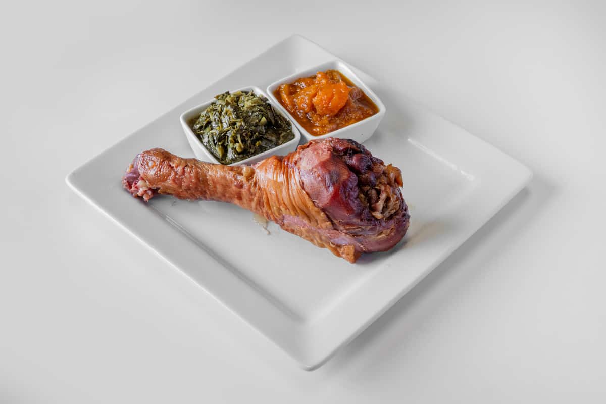 A stuffed smoked turkey leg with herb stuffing served alongside two side dishes on a white plate
