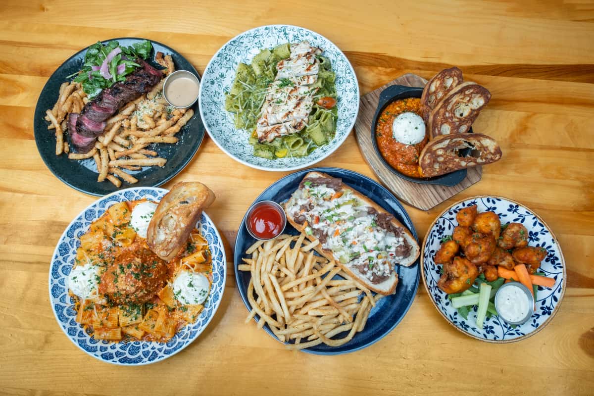 A variety of entrees on a table from Garp & Fuss featuring pasta, steak and sandwiches