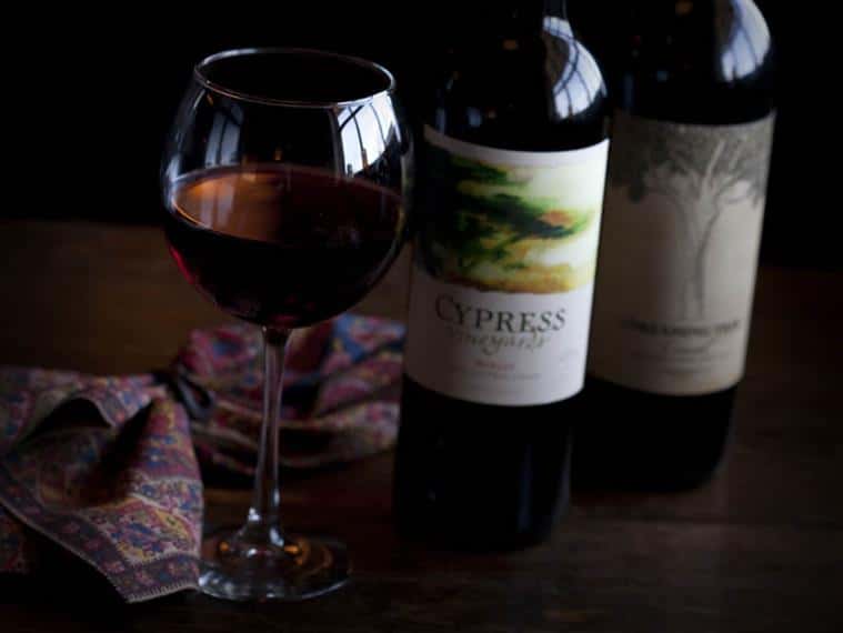 Two bottles and a glass of red wine on a wooden table.