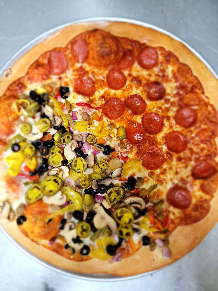 Loaded deluxe pizza from The John Hoover Inn, featuring pepperoni, mushrooms, black olives, and bright yellow jalapeno peppers on a golden crust.
