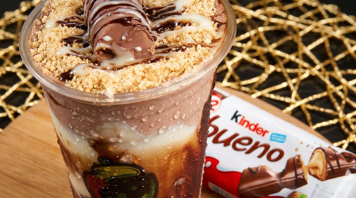 Chocolate milkshake with whipped cream, crushed wafers, and a piece of Kinder Bueno, next to a Kinder Bueno bar.
