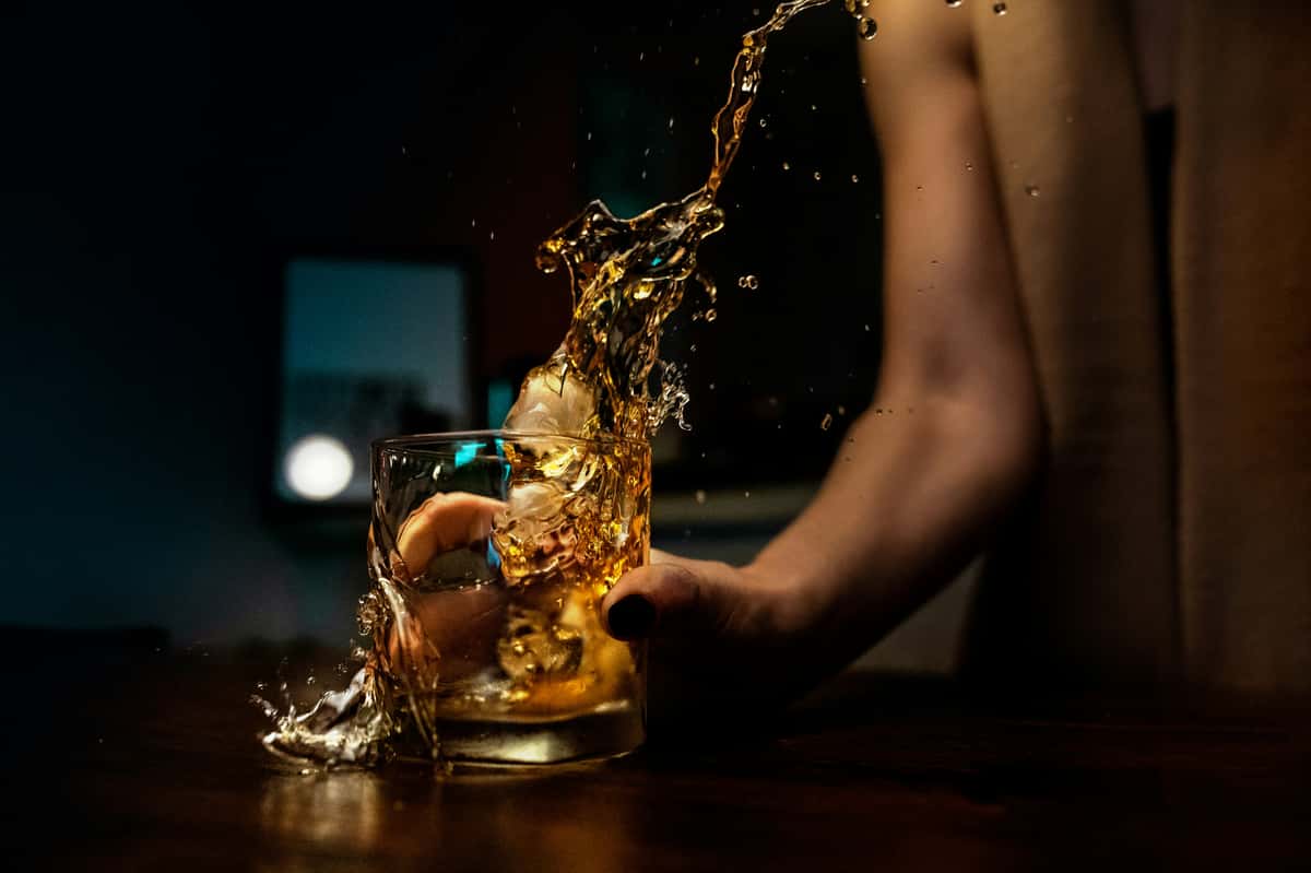 Whiskey cocktail splashing over ice in a rocks glass, dramatic bar scene with moody lighting