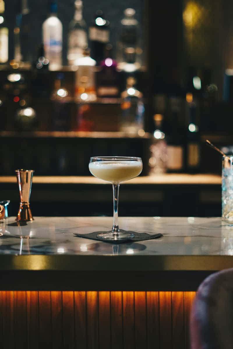 Elegant coupe glass cocktail on a marble bar top with warm ambient lighting and upscale lounge vibe