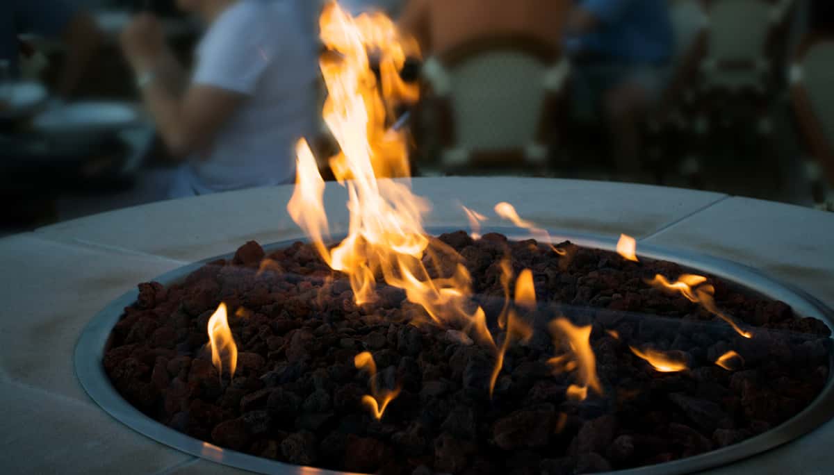 Outdoor fire pit with flames burning over dark stones.