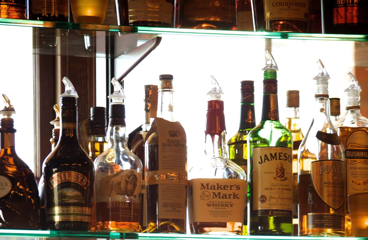 Bar shelf filled with assorted liquor bottles behind glass.