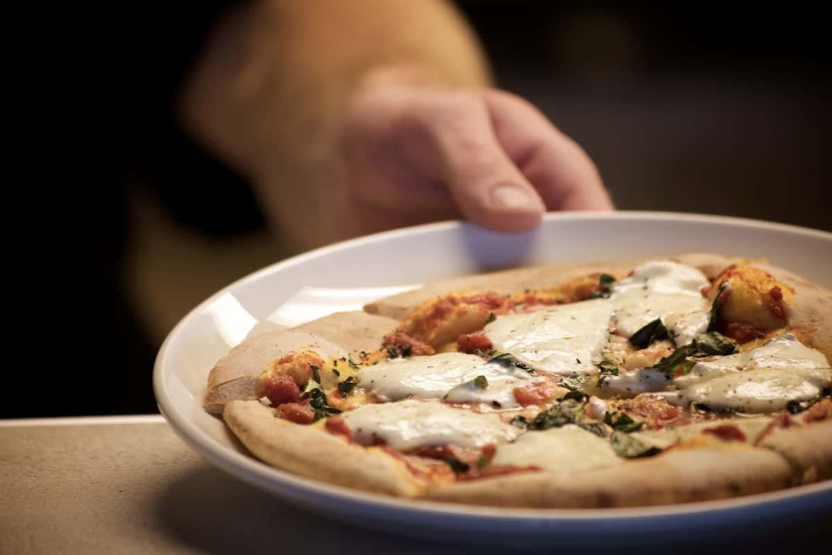 Small pizza topped with melted cheese and herbs on a white plate.