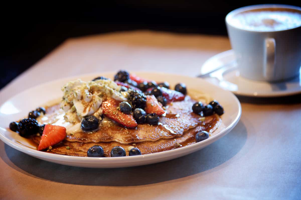 Pancakes topped with blueberries and strawberries served with a cup of coffee.