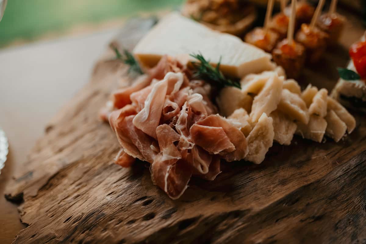 Close-up view of a gourmet cheese and prosciutto platter on rustic wooden board.